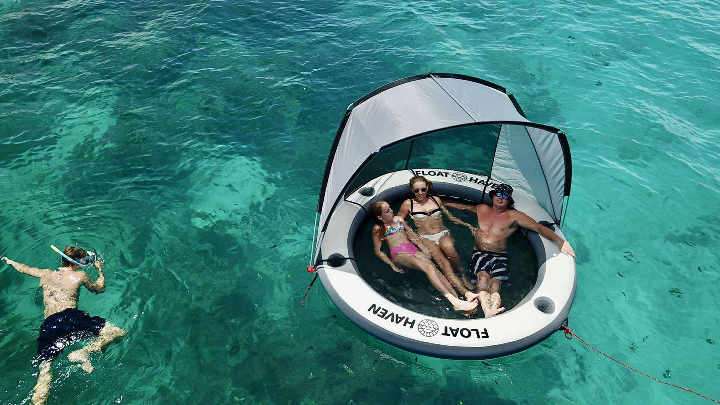 Family relaxing on a Float Haven inflatable floating island while snorkeling in clear turquoise water.