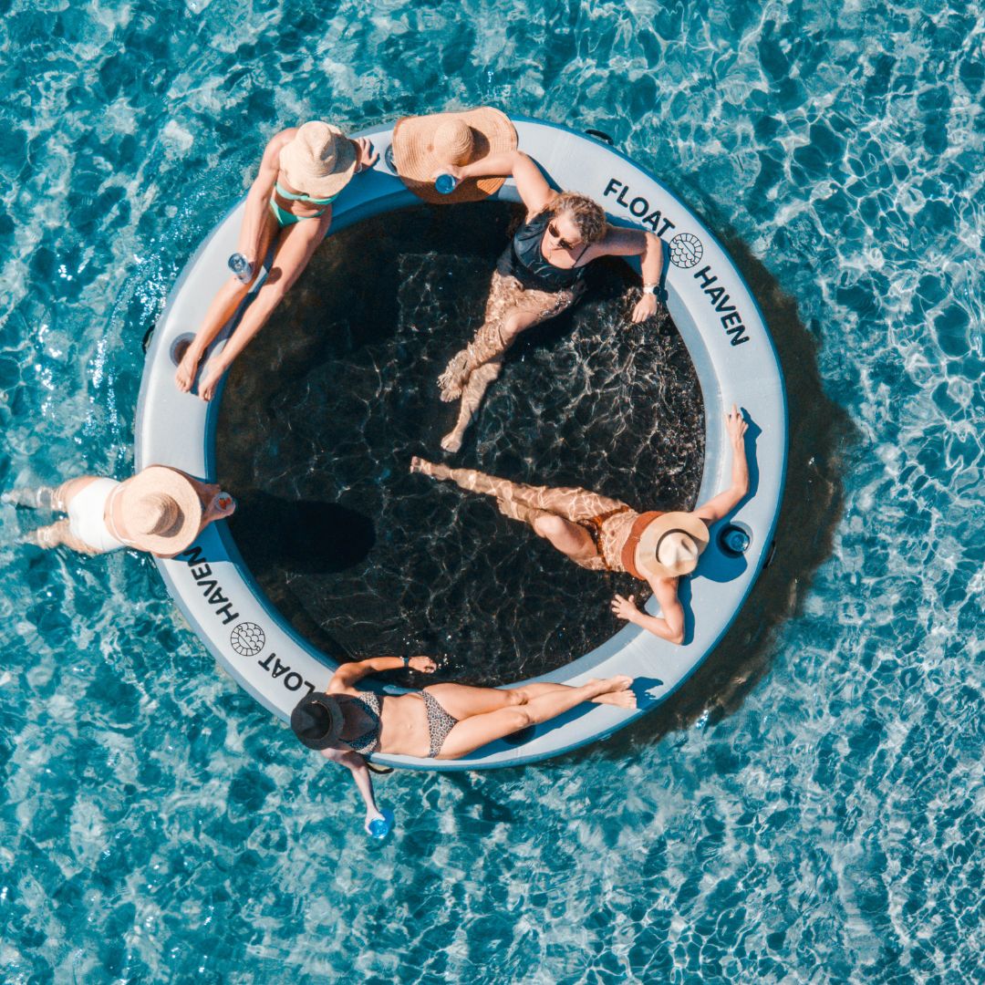 People relaxing on a circular inflatable Float Haven floating island  platform in clear blue water.