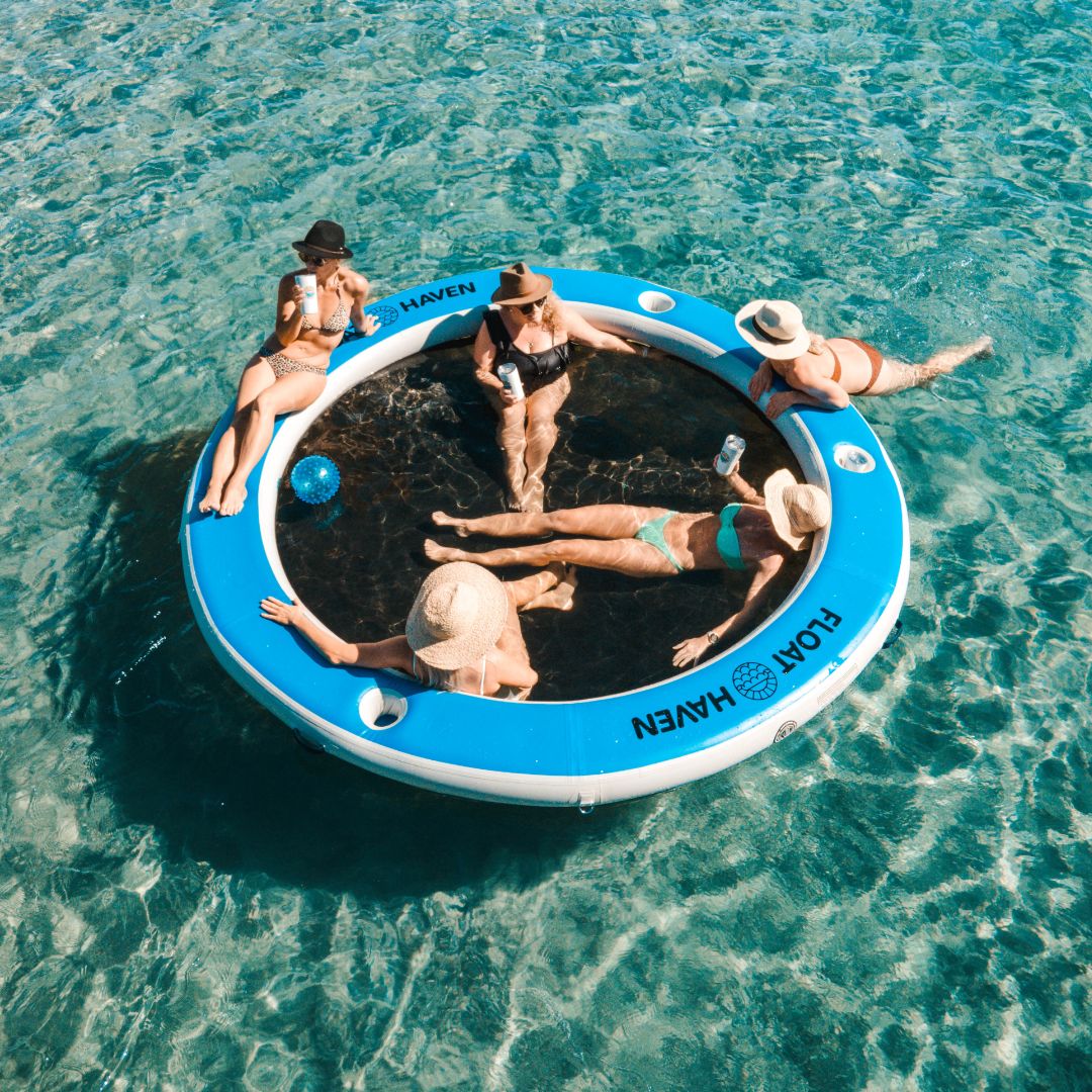People relaxing on a circular inflatable floating island in clear blue water.