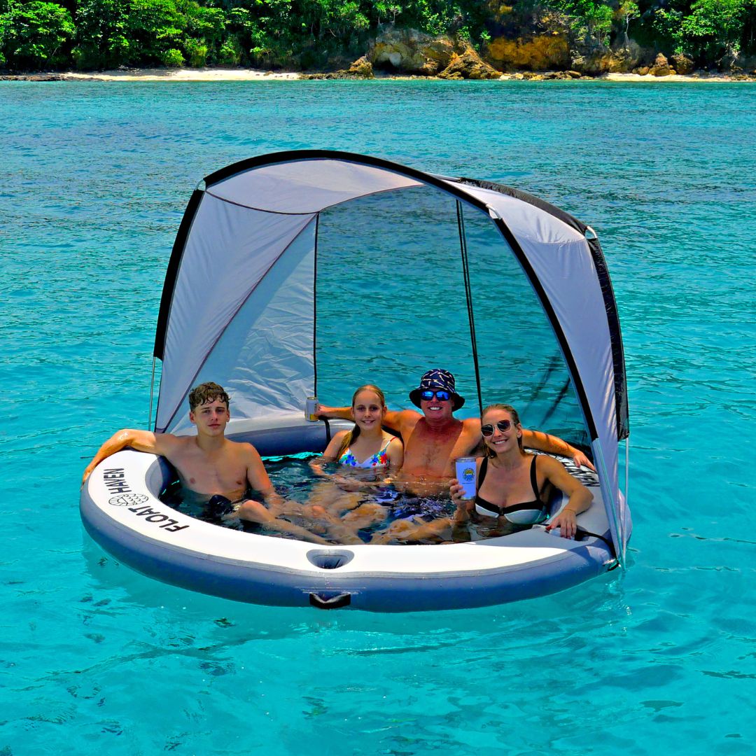 People enjoying a sun sheltered inflatable pool toy in clear blue water with a tropical island in the background.